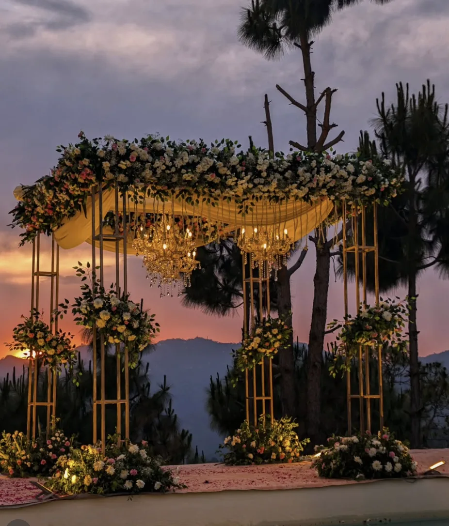 Floral mandap with hanging chandeliers against a mountain sunset at a hillside destination wedding